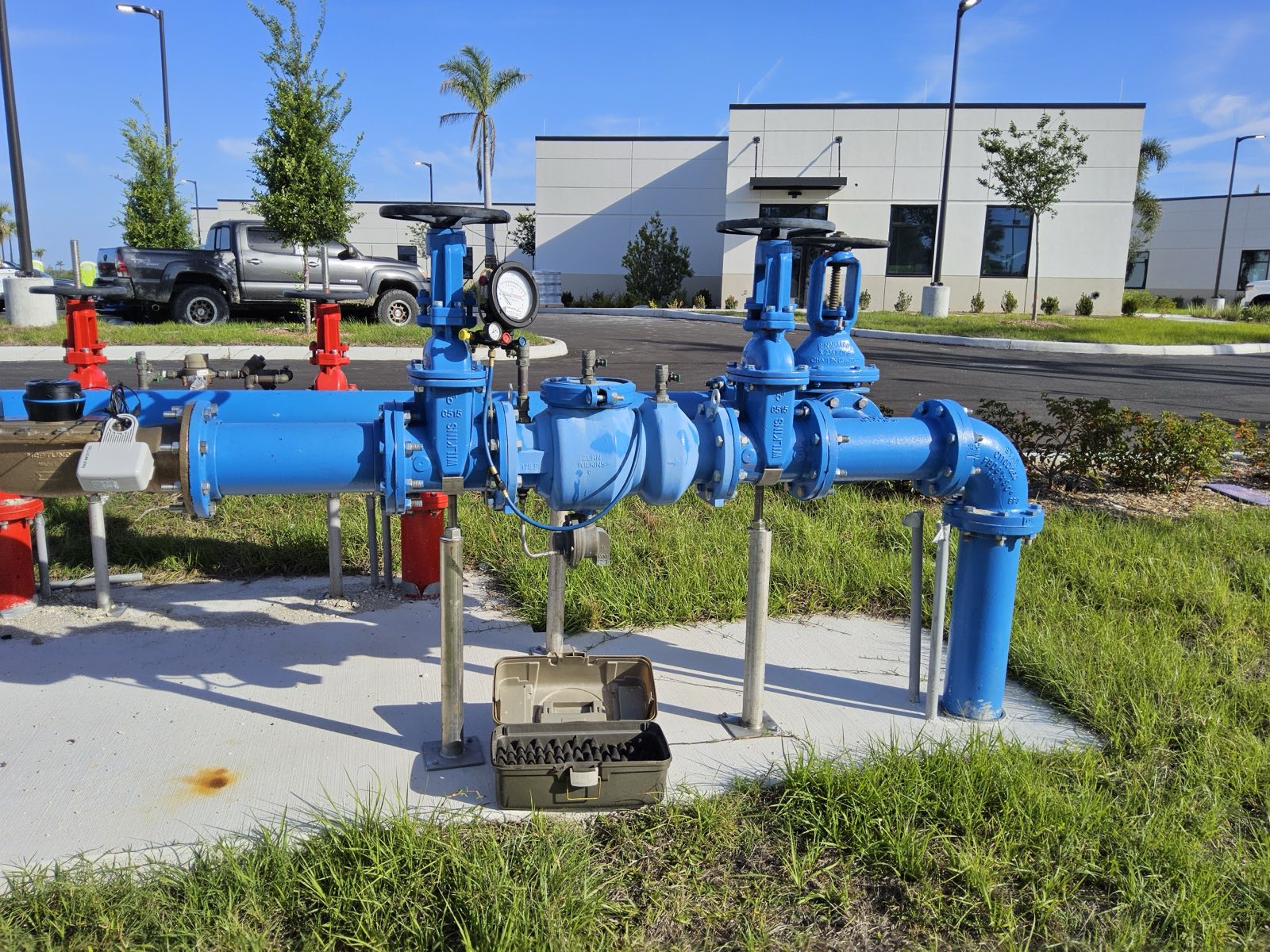 Commercial 4-inch reduced-pressure backflow assembly mounted on a white stucco exterior wall in Florida.