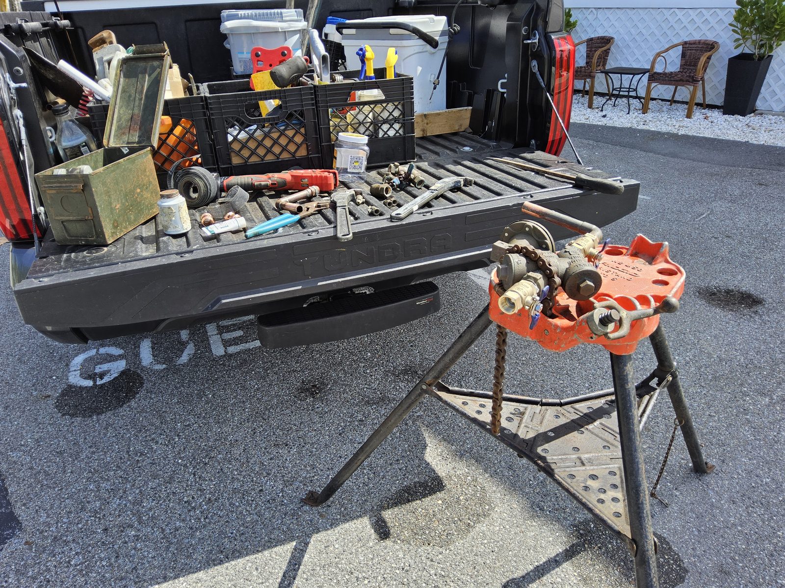 A Plus Backflow Testing field setup — Toyota Tundra tailgate loaded with fittings, brass nipples, and tools, with a Wilkins RPZ assembly mounted on a chain pipe vise mid-service.